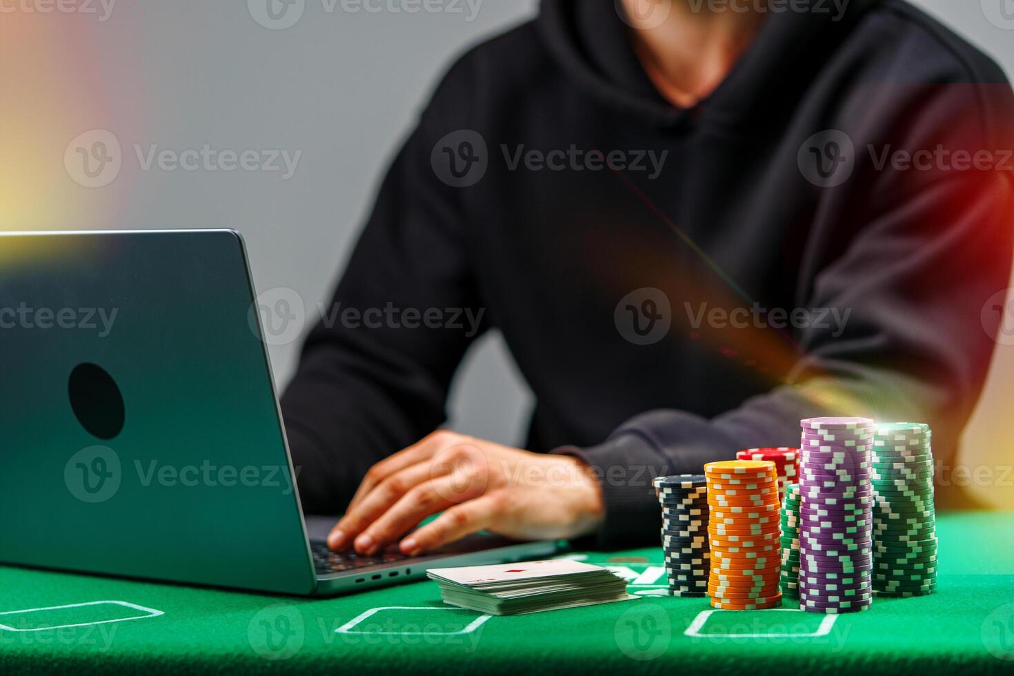 A player engages with online poker on a laptop, surrounded by colorful chips and playing cards on a green table photo