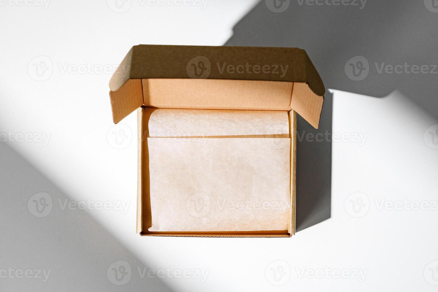 A small, empty cardboard box with unwrapped parchment resting inside on a bright, sunlit table photo