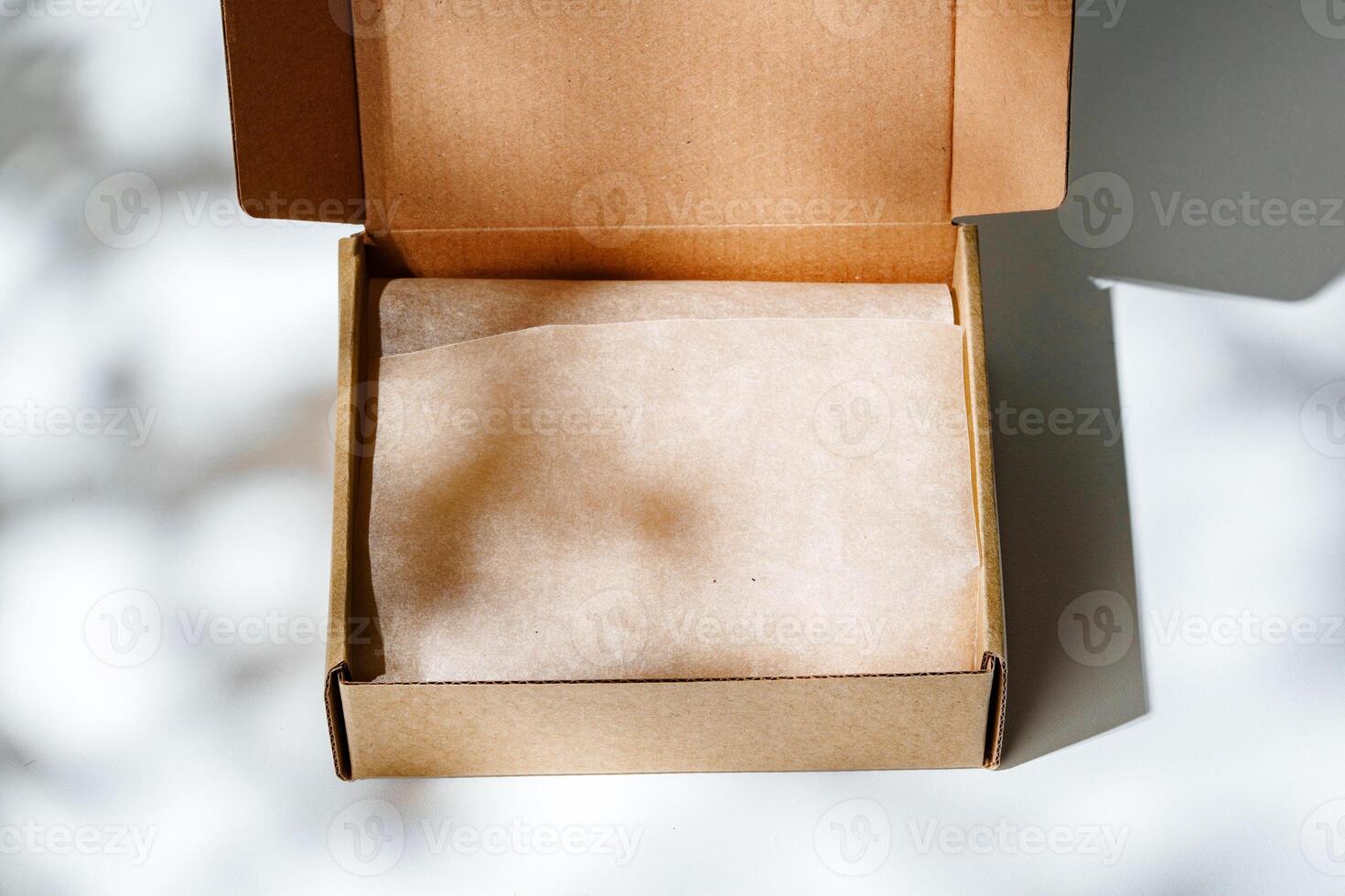 A small, empty cardboard box with unwrapped parchment resting inside on a bright, sunlit table photo