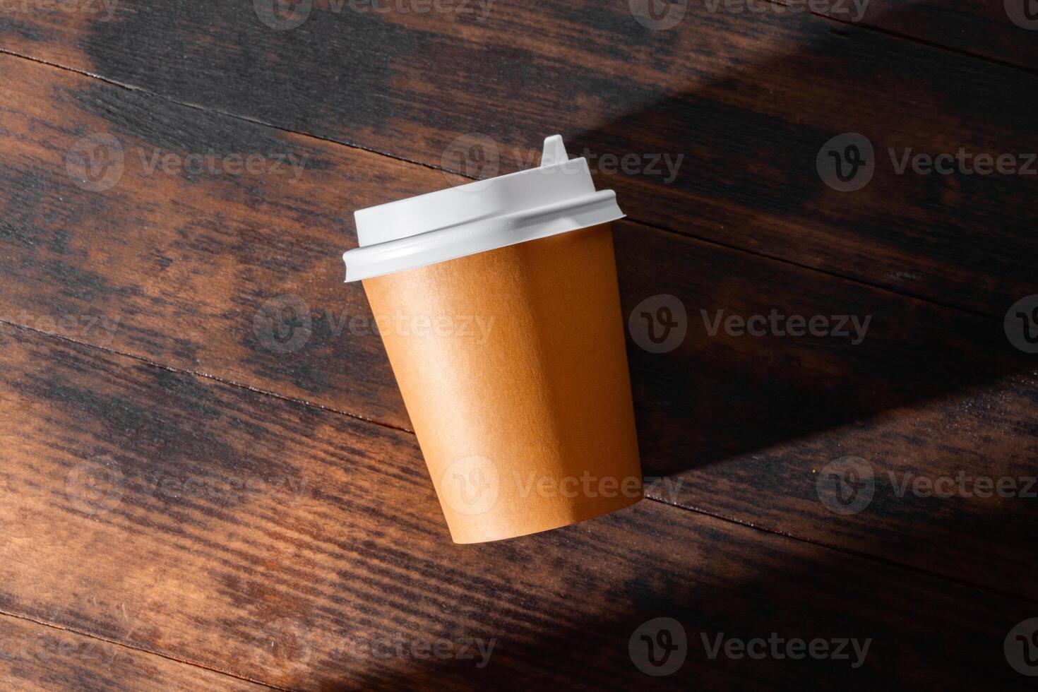 A takeout coffee cup rests on a wooden table, highlighting its simple design and warm tones in soft natural light photo