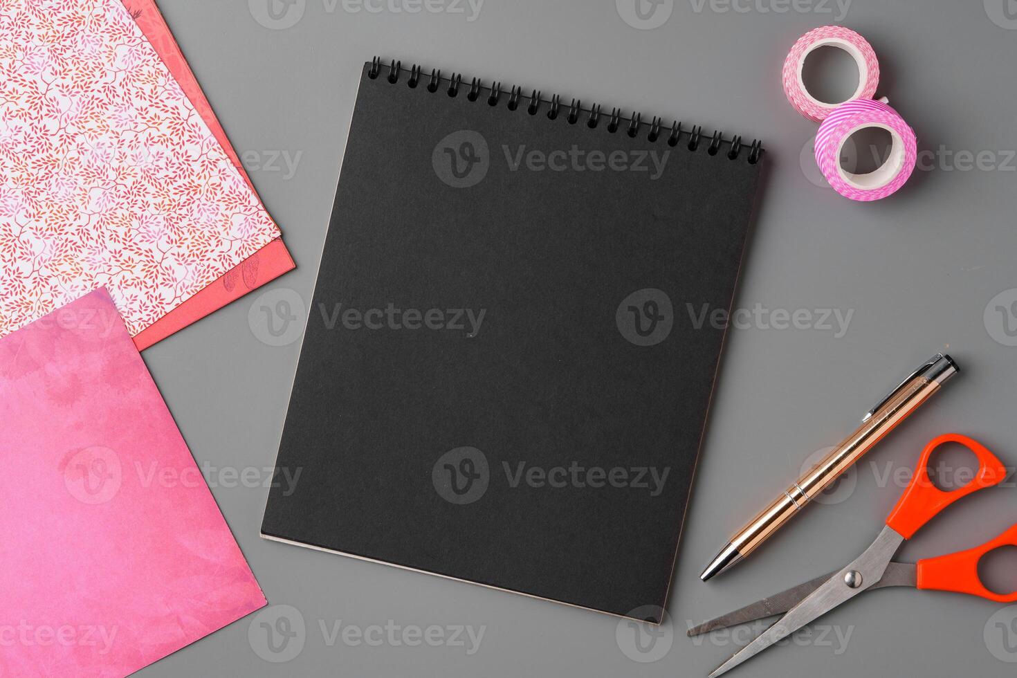 Crafting supplies arranged on a gray surface with a blank notebook, scissors, washi tape, and colorful embellishments photo