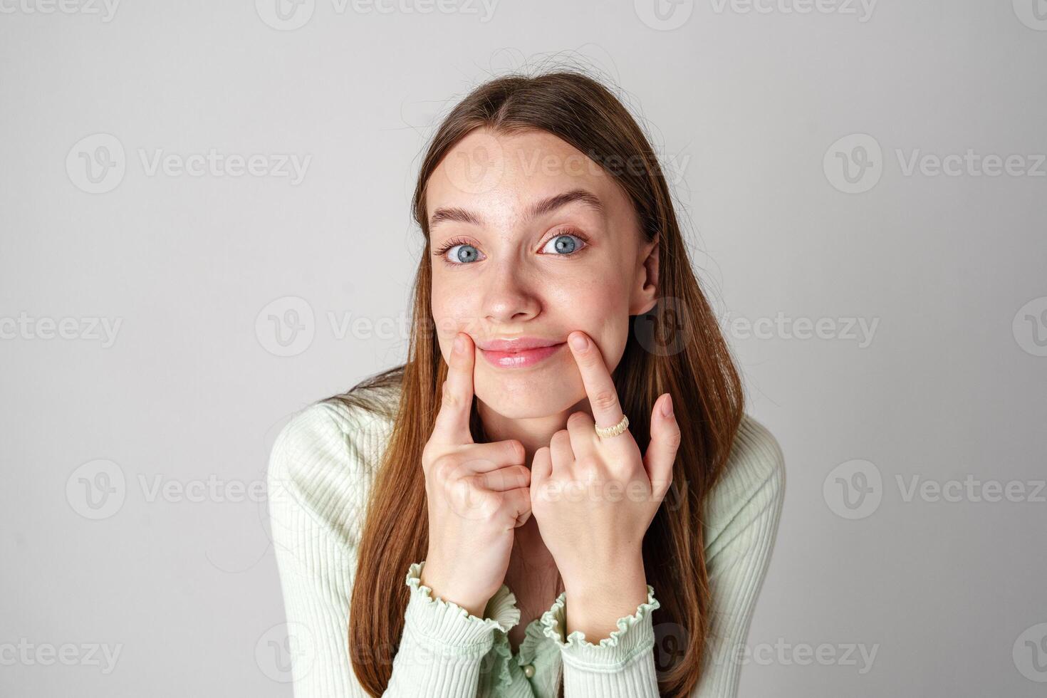 Young Woman With Long Brown Hair Smiles and Touches Her Cheeks photo