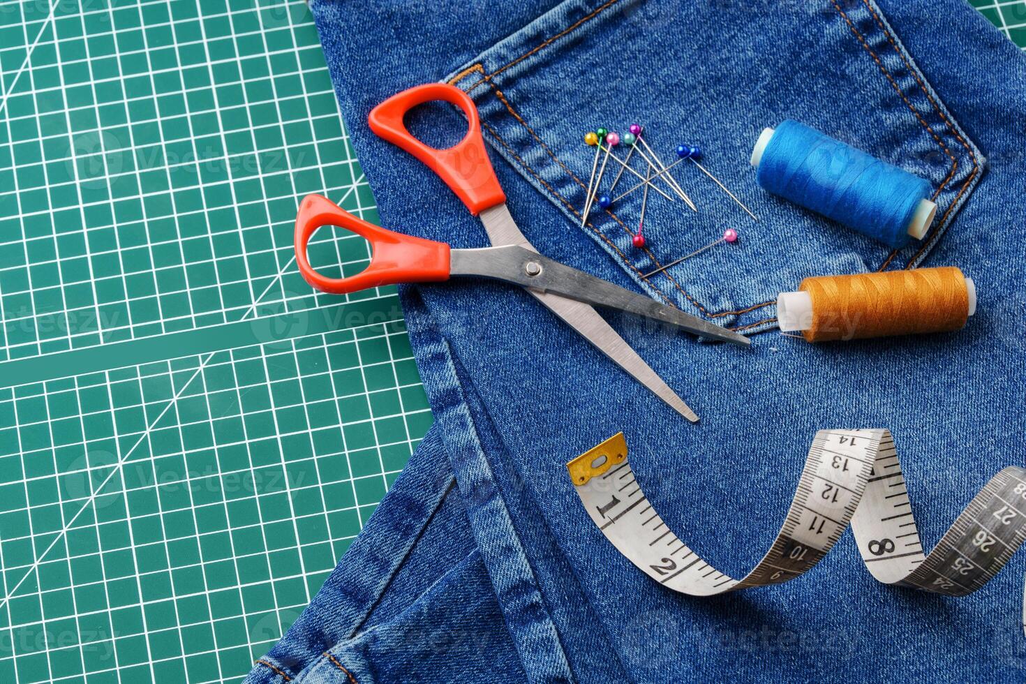 Sewing tools on a cutting mat with denim and thread spools in a craft workspace photo