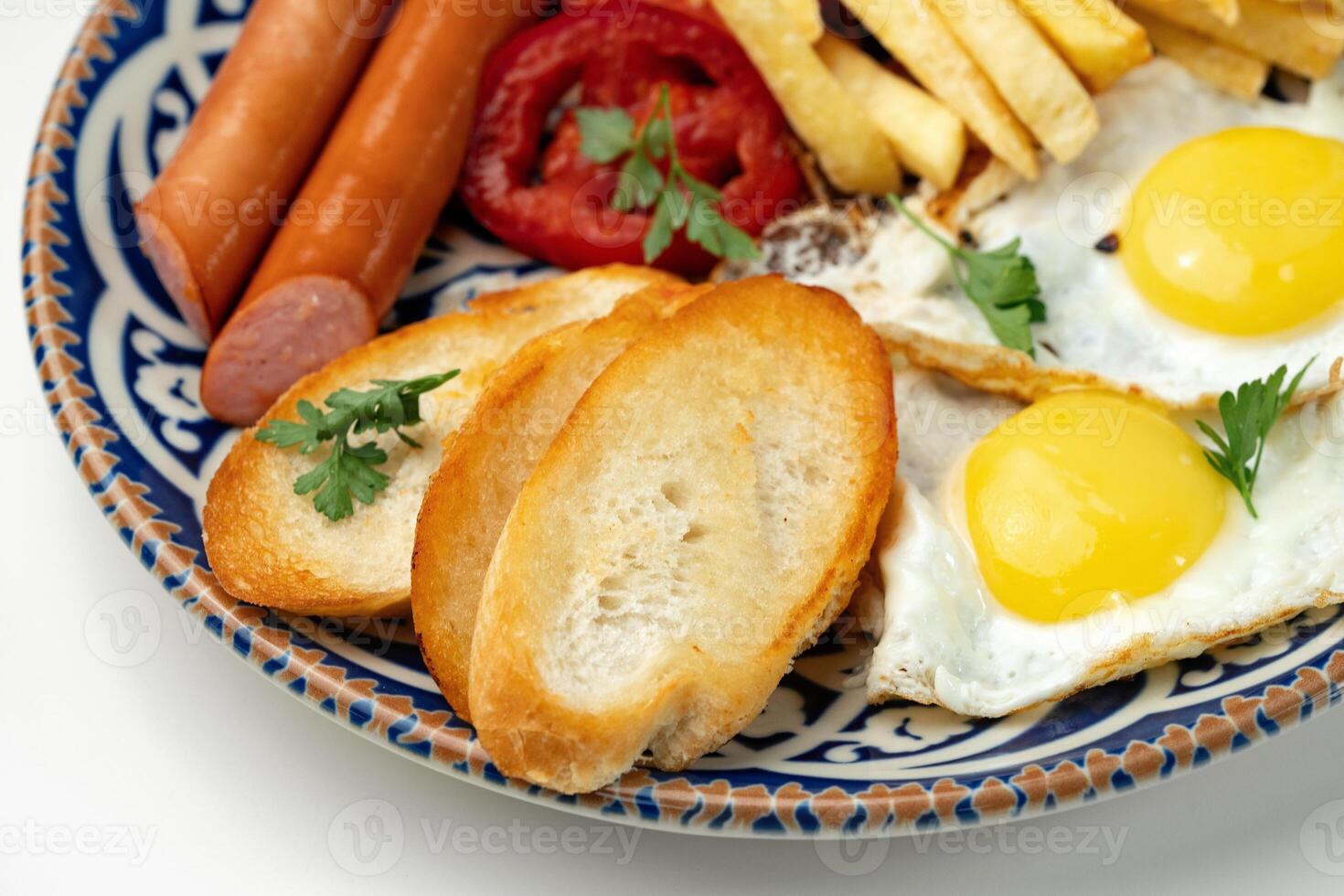 Breakfast plate with fried eggs, sausage, tomatoes, and fries served on a decorative blue plate photo
