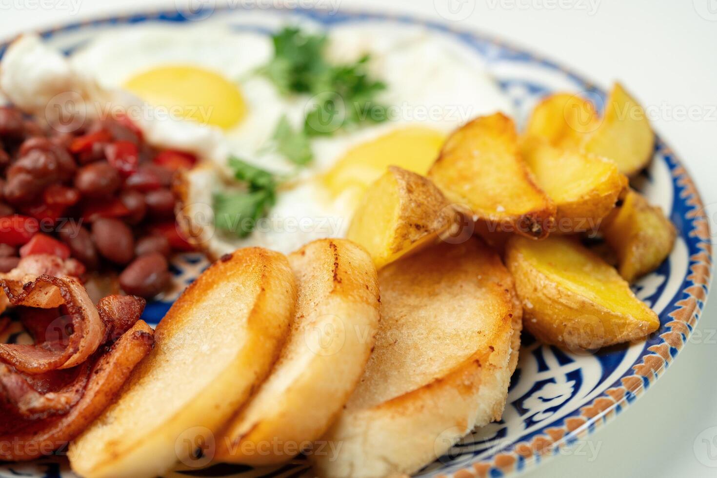 Delicious breakfast plate featuring eggs, beans, bacon, and potato wedges served on a decorative dish photo