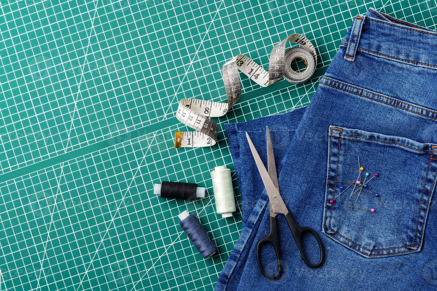 Sewing tools on a cutting mat with denim and thread spools in a craft workspace photo
