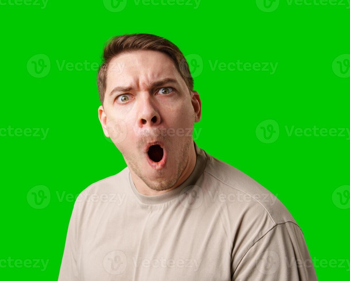 A surprised man stands in front of a bright green screen, expressing shock with his mouth open photo