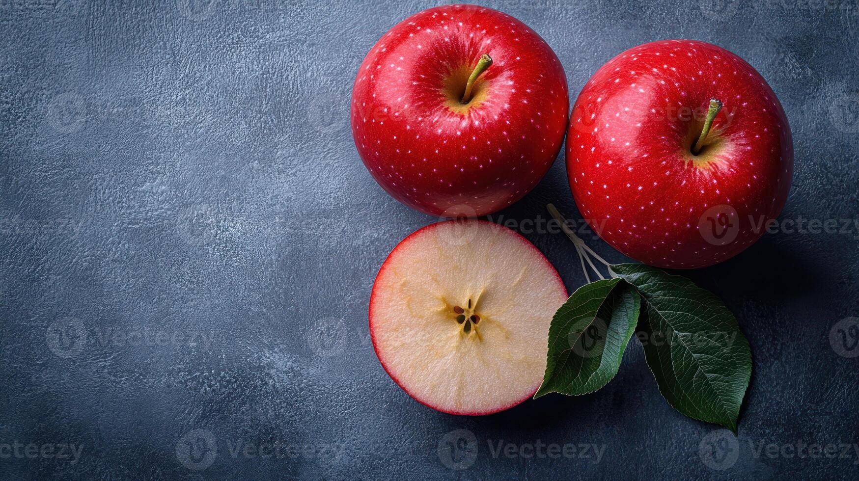 Two vibrant red apples rest on blue backdrop, one sliced in half to show its core photo