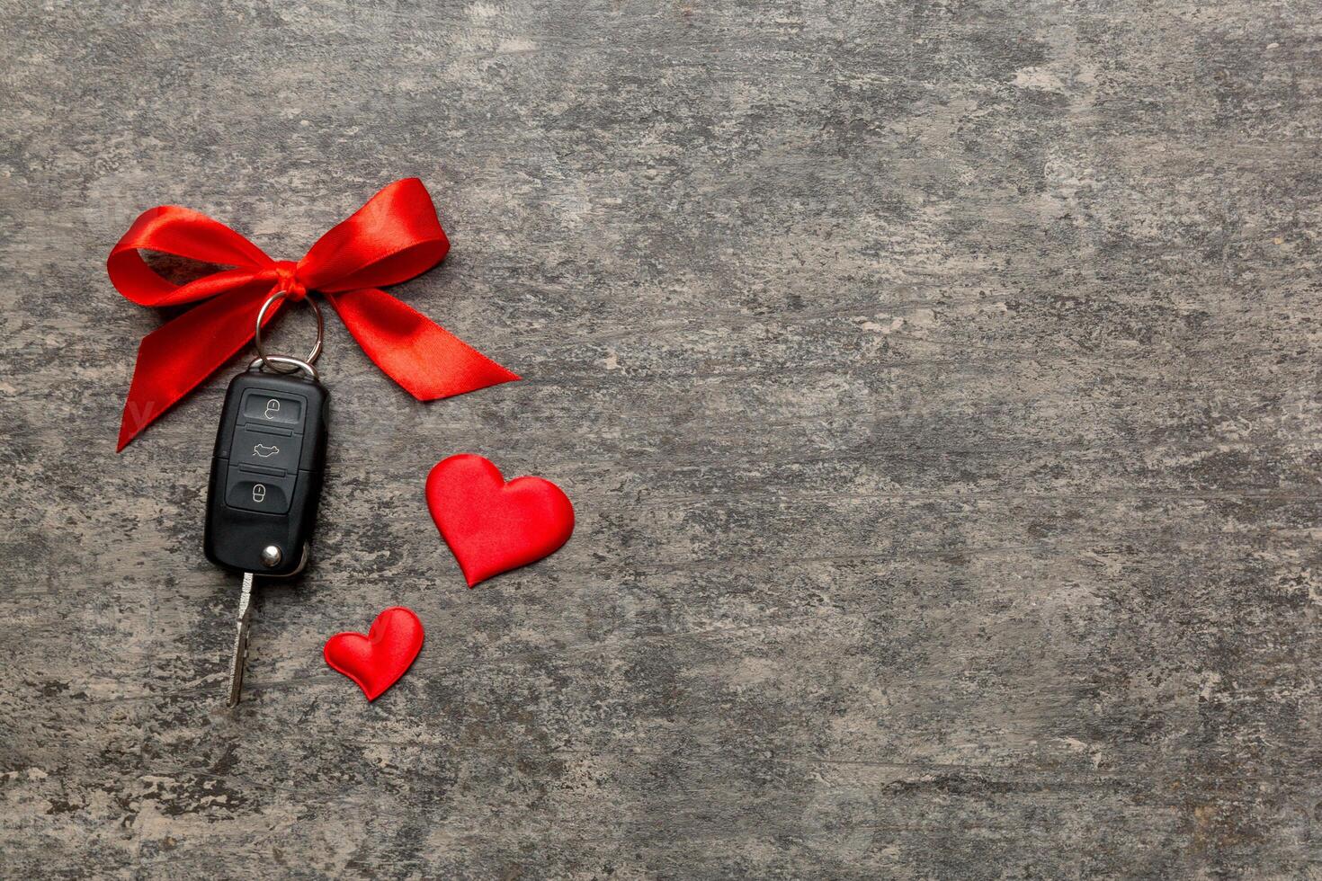 Car key a red bow and a heart on Colored table. Giving present or gift for valentine day or christmas, Top view with copy space photo