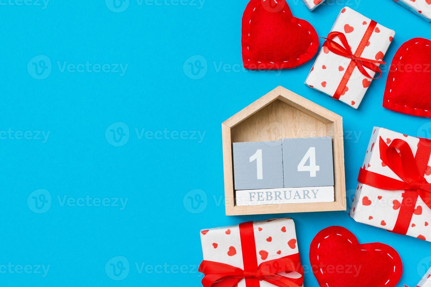 Holiday composition of gift boxes, wooden calendar and red textile hearts on colorful background with empty space for your design. photo
