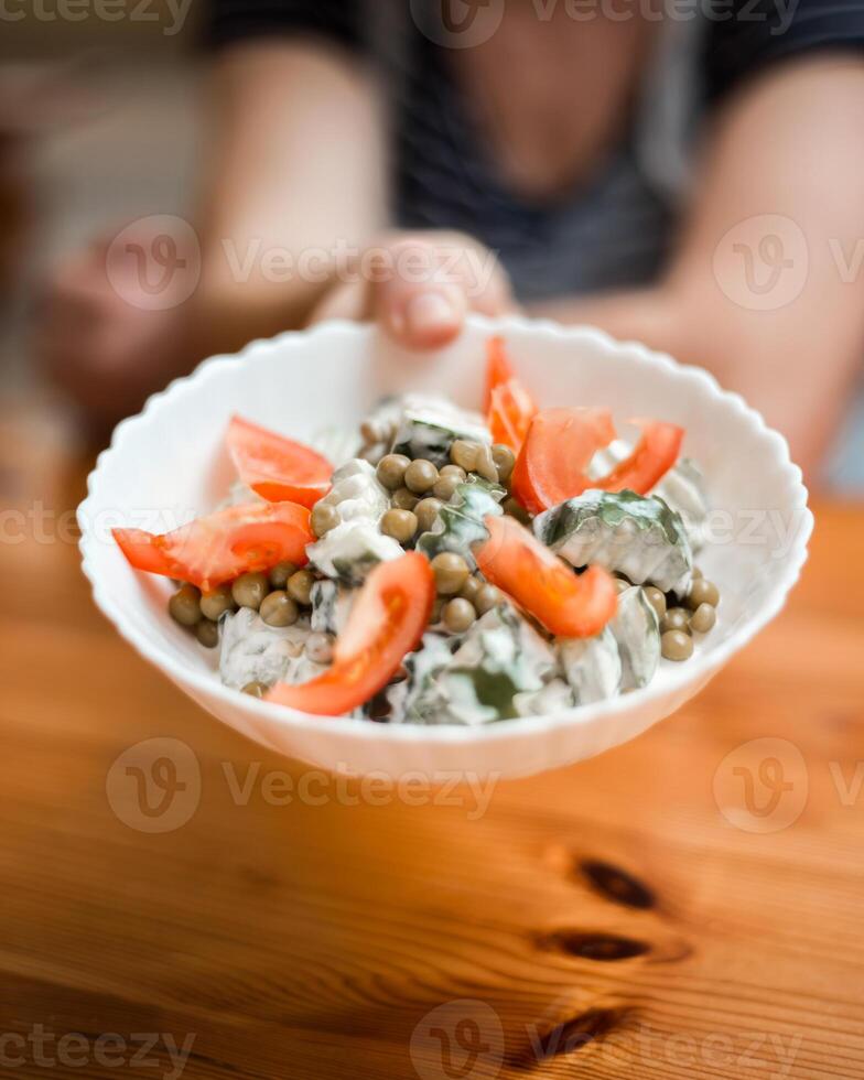 Hand Holding Bowl of Tomato, Pea, and Cucumber Salad on Wooden Table photo