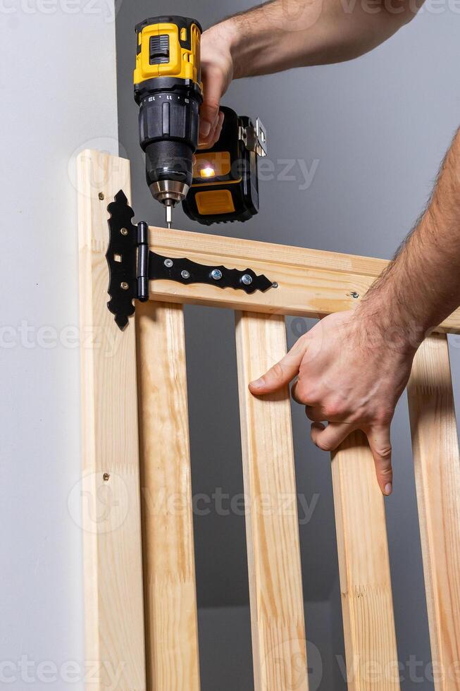 Hands Using Yellow and Black Cordless Drill on Wooden Gate Hinge photo
