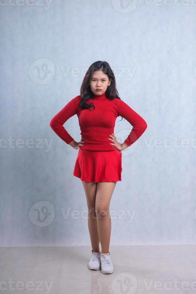 full length charm of young female wearing red sweater, standing pouting looking at camera both hands holding waist, isolated on white background photo