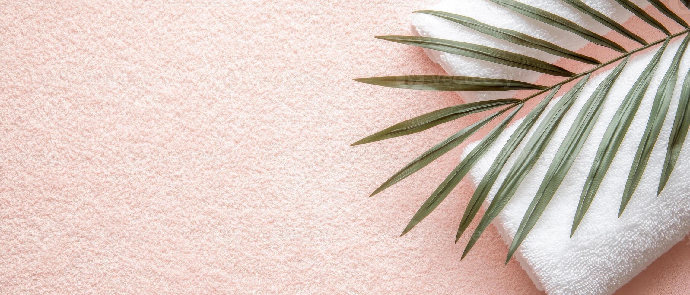 soft white towel rests on pastel pink surface, accompanied by green palm leaf, creating serene and relaxing atmosphere perfect for sunbathing photo