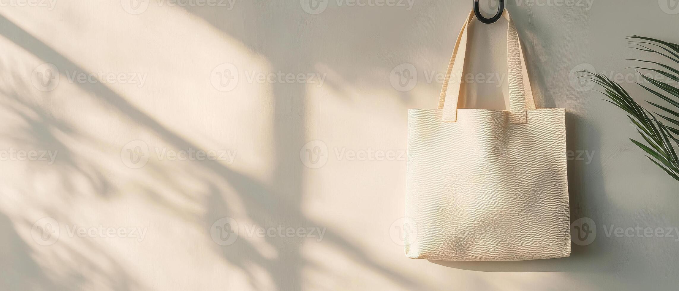 minimalist reusable tote bag hangs against soft wall, casting gentle shadows. serene atmosphere is enhanced by presence of nearby plant, creating calming scene photo