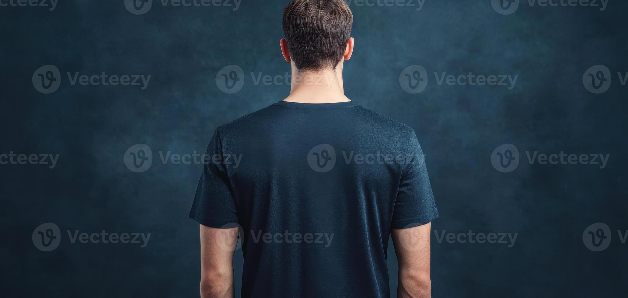 man wearing navy t shirt stands against dark background, showcasing back view of shirt. clean display highlights fabric and color, creating modern and stylish look photo
