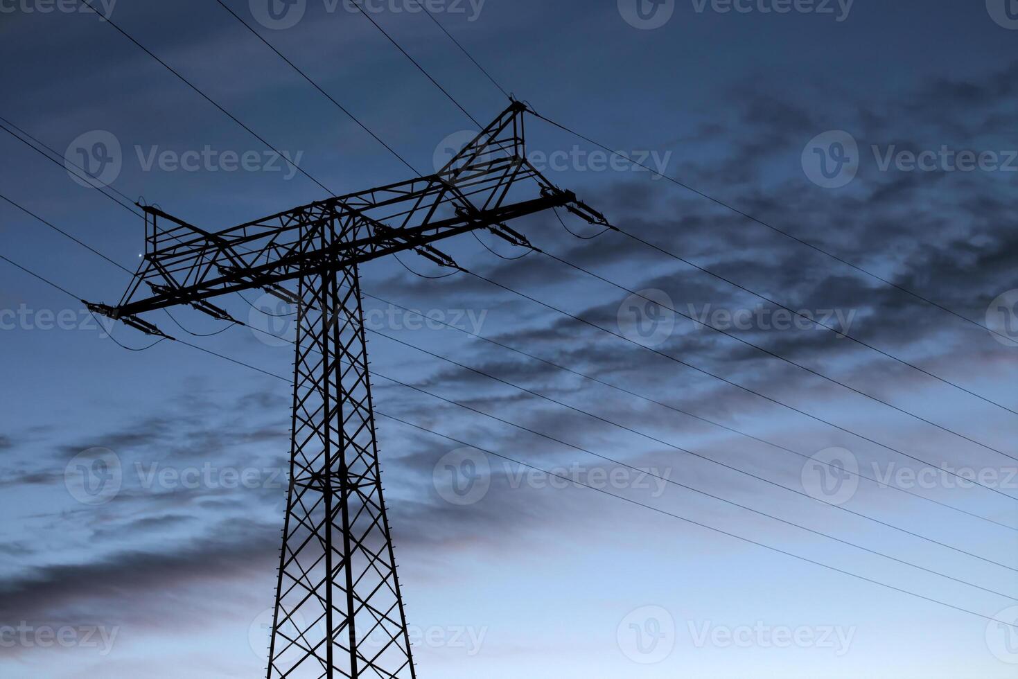 View on a high voltage power line in the evening. The blue sky contains clouds parallel to the power line frame. photo