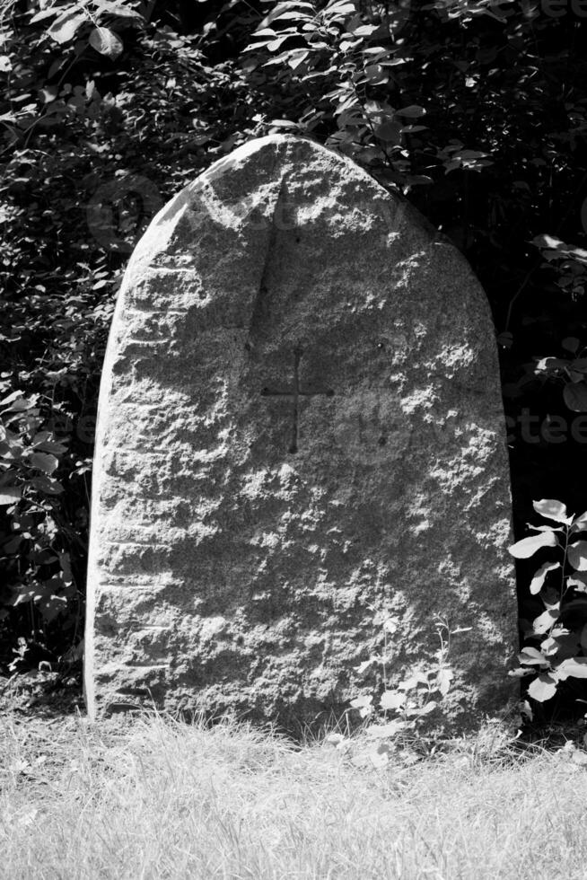 Black and white shot of an old tombstone with a simple cross carved into it. photo