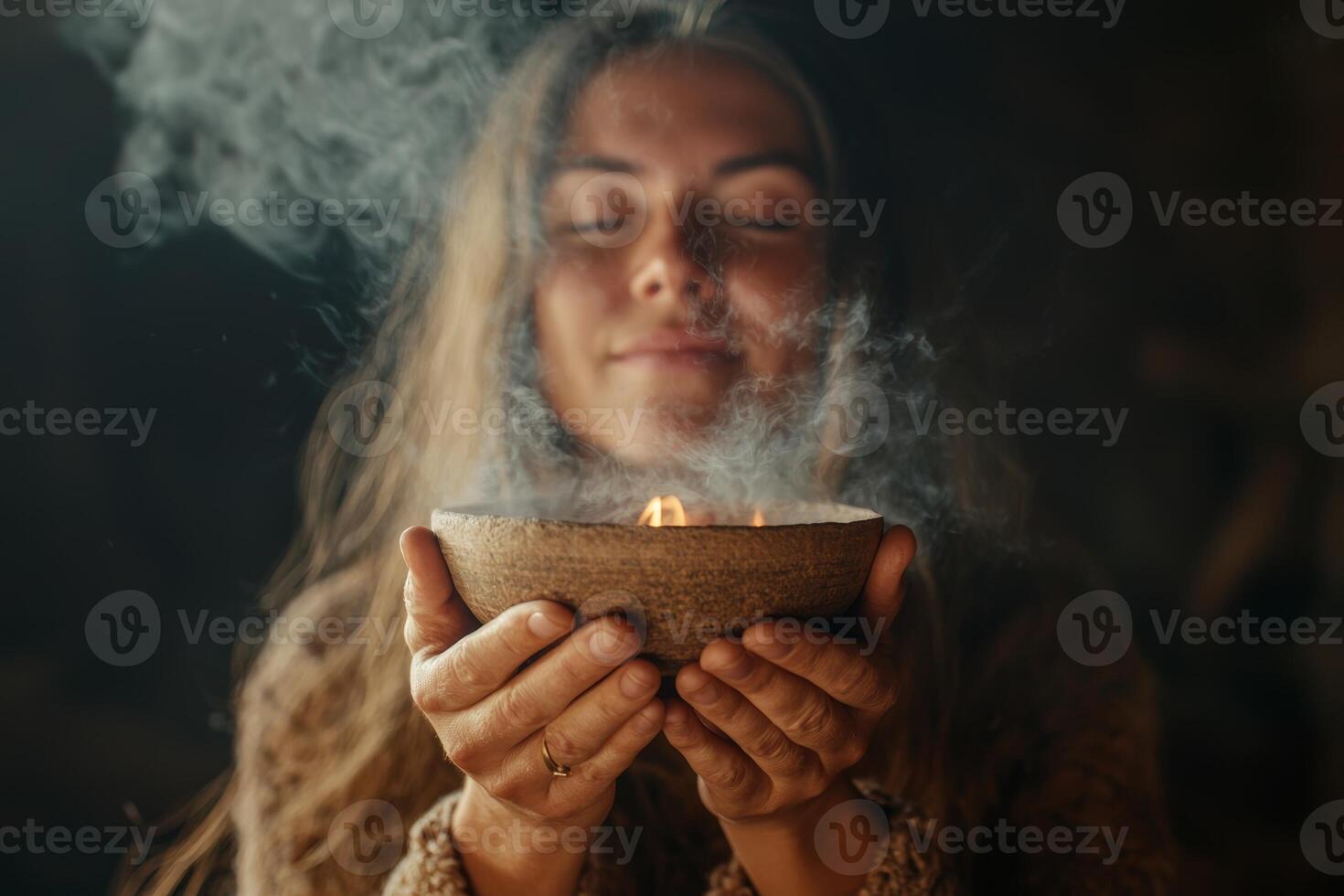 A woman offers a bowl of fragrant herbs while meditating in a serene, dimly lit space during a peaceful afternoon moment photo