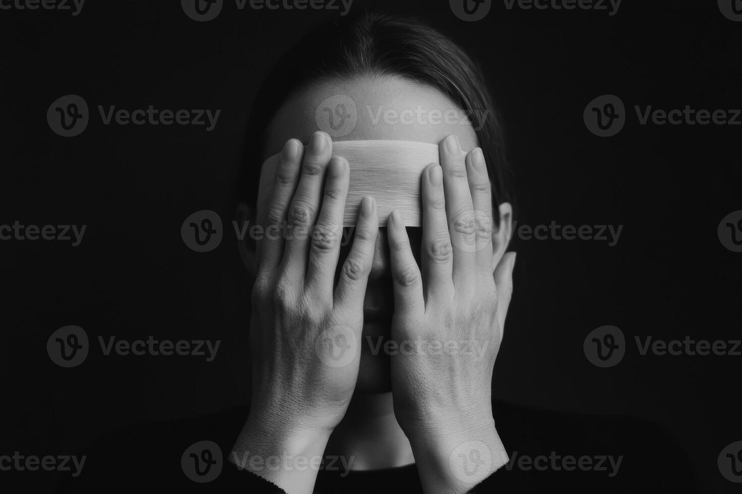 A person with covered eyes holding a wooden object in a dark setting, conveying emotions of introspection and contemplation photo