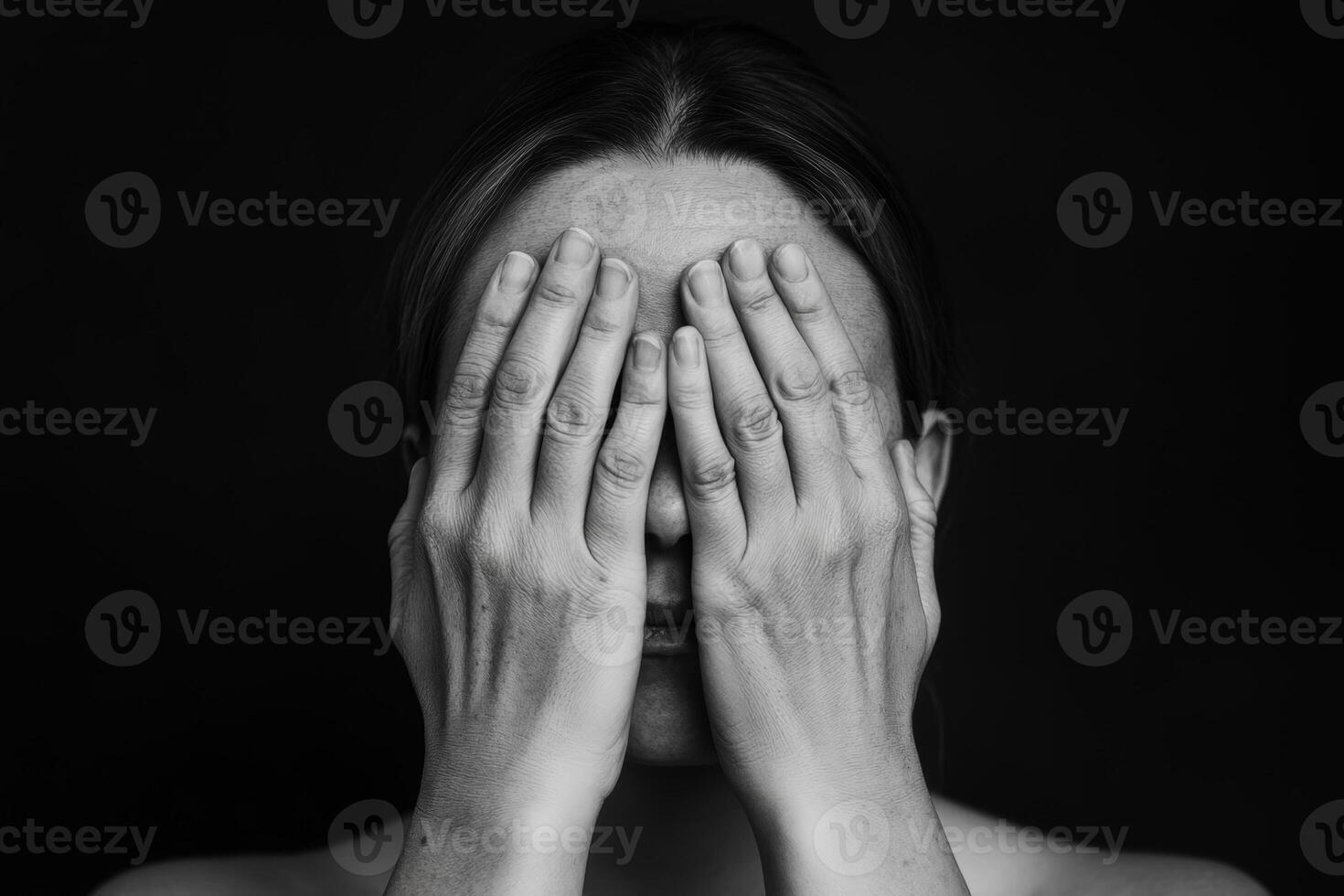 A woman covers her face with her hands in a thoughtful moment against a dark backdrop in a serene indoor setting photo