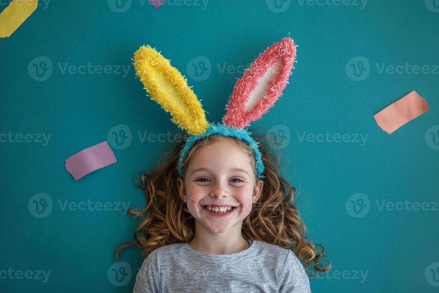 A joyful girl wearing colorful bunny ears smiles on a bright turquoise background with playful decorations around her photo