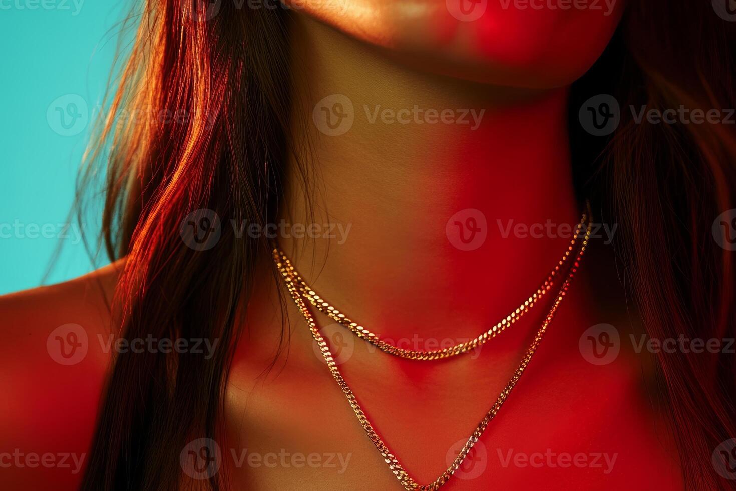 A close-up view of layered gold necklaces worn by a person with long hair illuminated by vibrant red and blue lighting photo