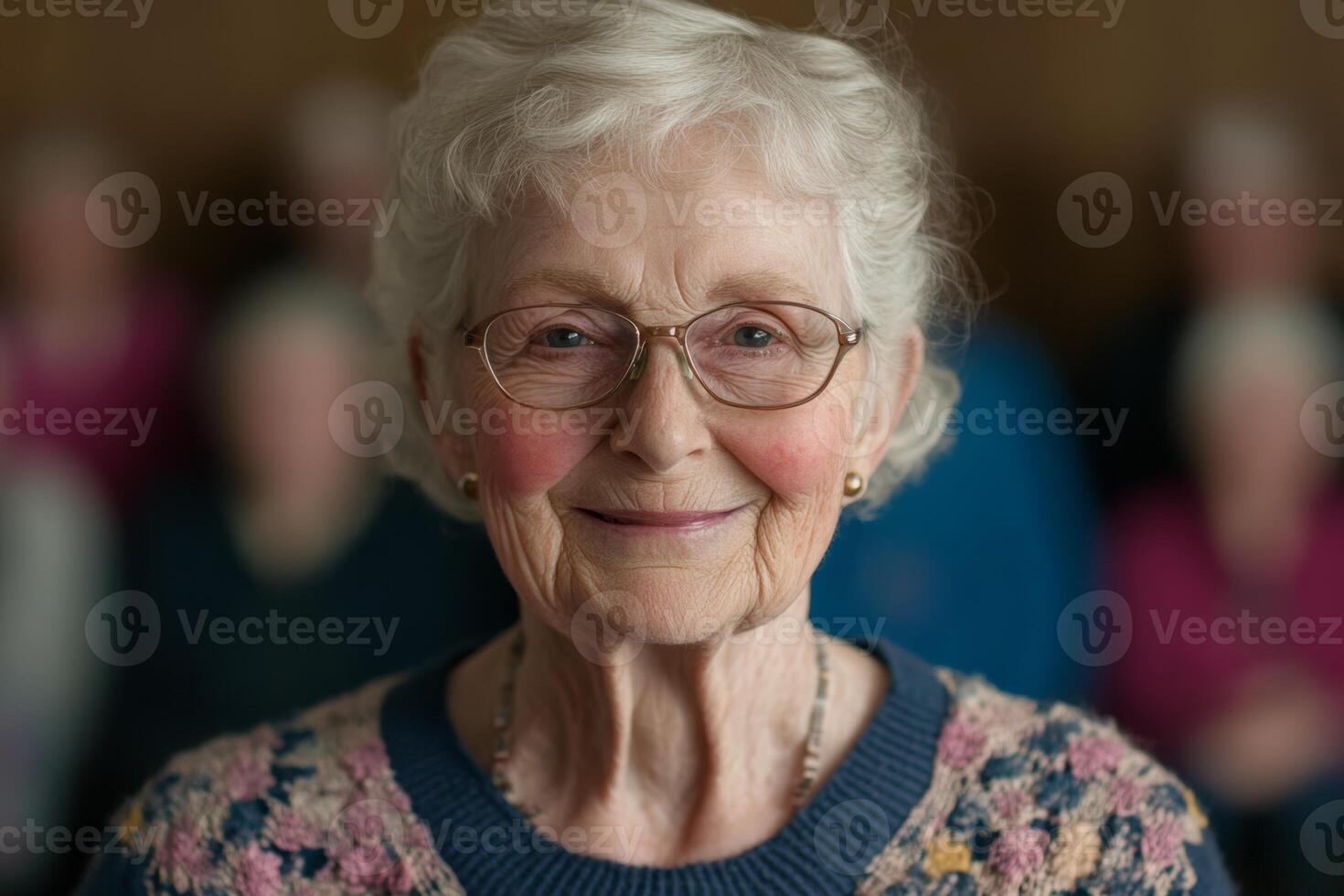 Cheerful older woman smiling warmly at the camera in a cozy indoor setting with friends behind her, captured during a gathering photo