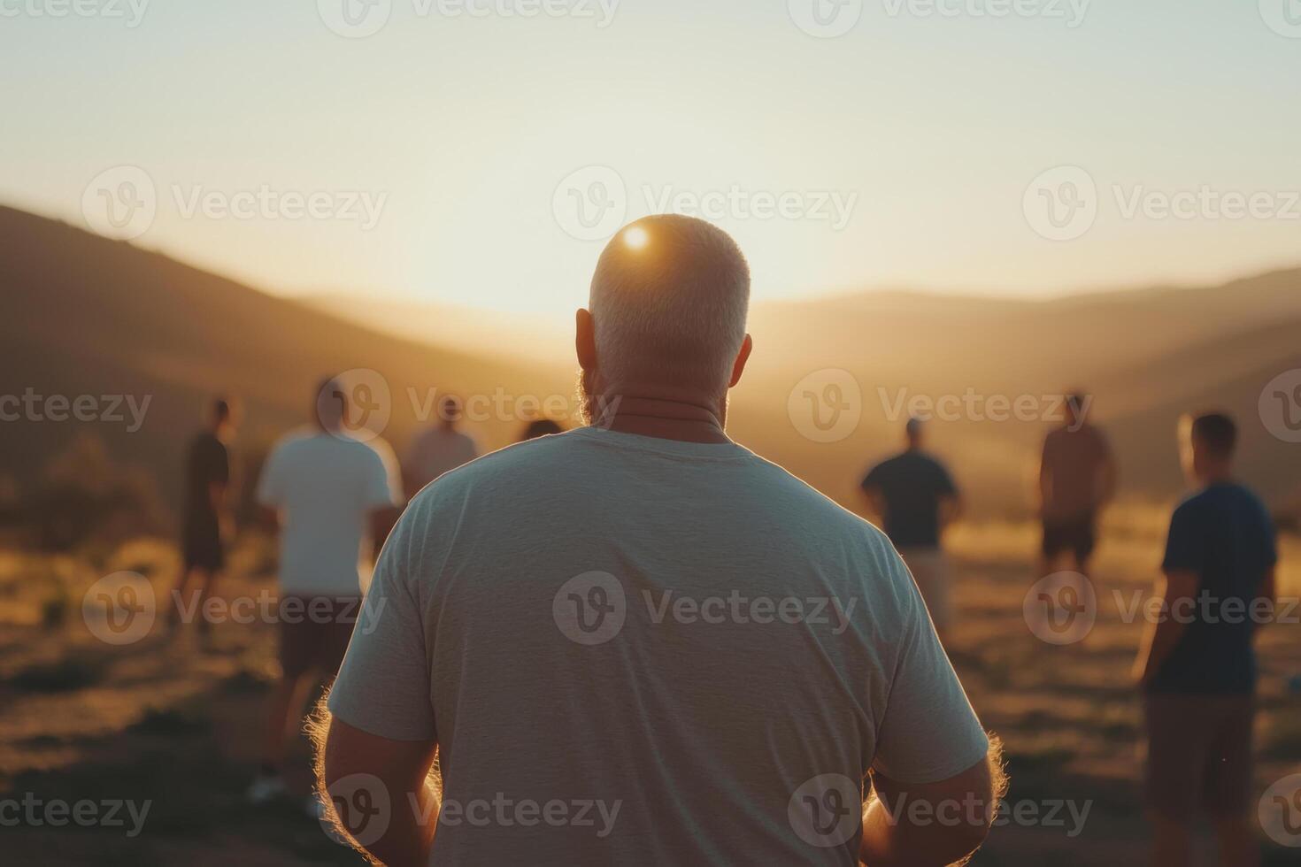 A group of people gathers at sunset for meditation in a serene outdoor setting among rolling hills photo