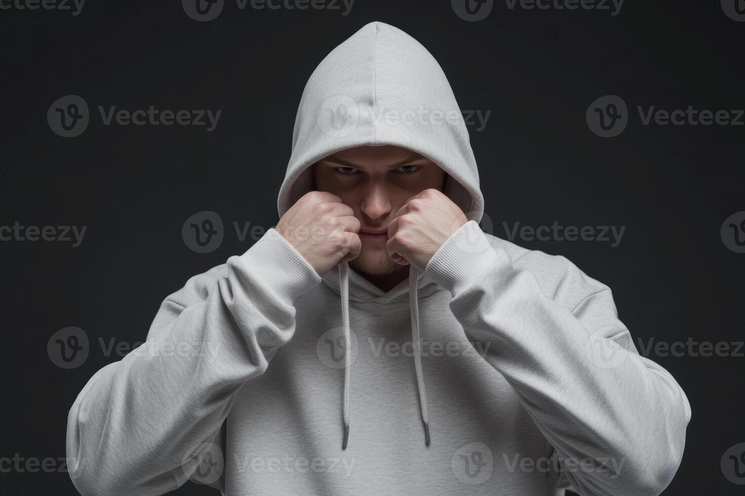 A young man wearing a gray hoodie prepares to fight in a dramatic indoor setting with a dark background and focused expression photo