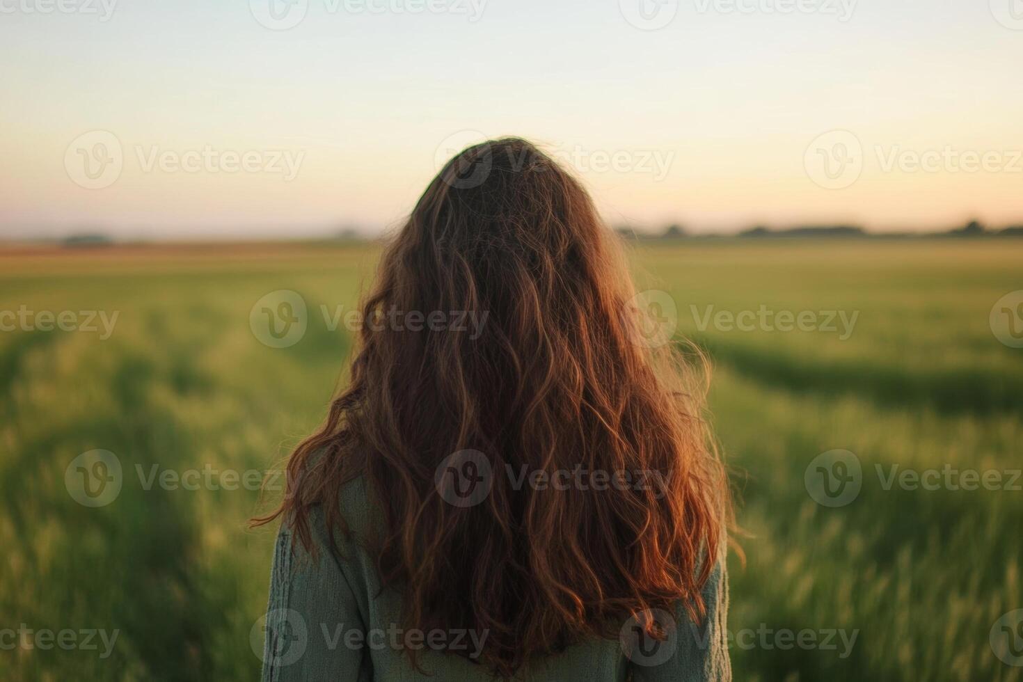 A person with long hair stands in a green field at sunset, enjoying the peaceful landscape and warm glowing light photo