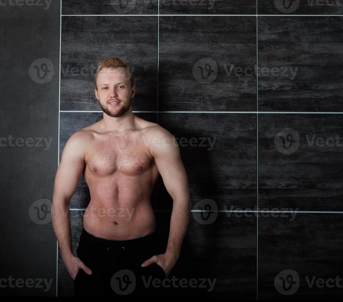 Handsome muscular male model near black wall photo