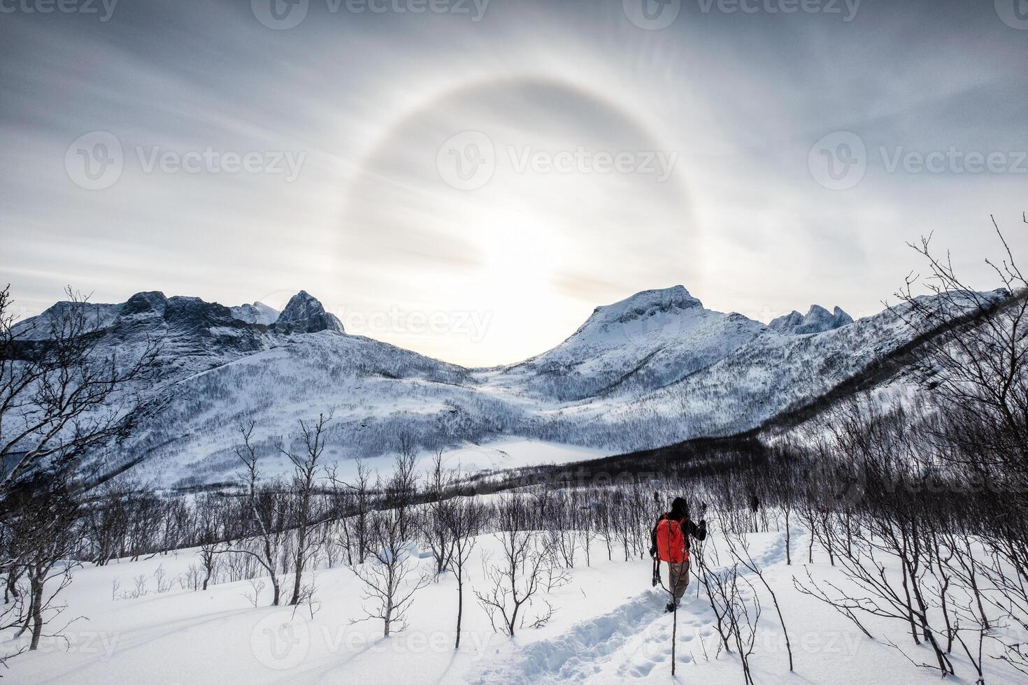Backpacker climbing on snow peak with Sun halo on mountain range photo