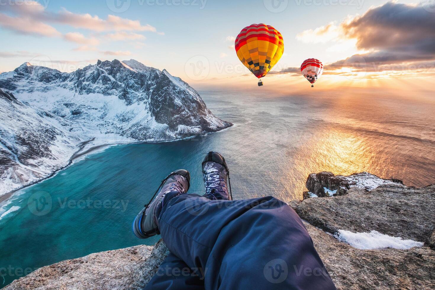 Man hiker cross legs sitting on rock ridge with hot air balloon flying on ocean photo