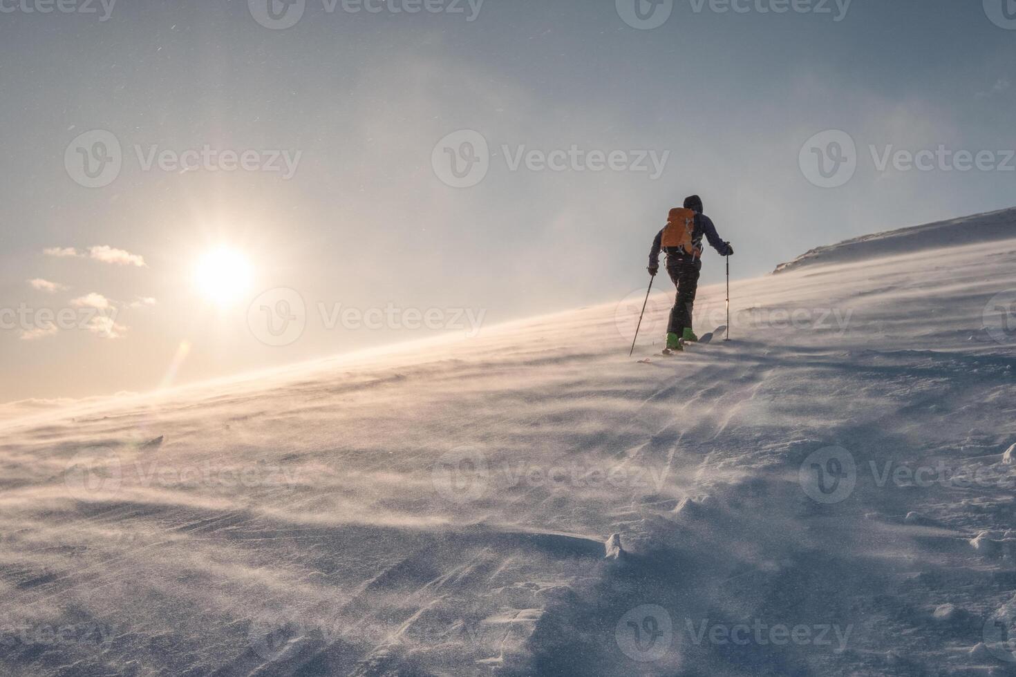 Skier with backpacker hiking on snow hill at sunset photo