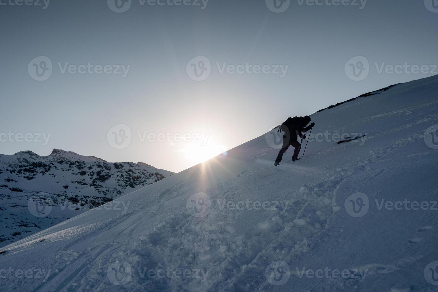Man mountaineer climbing on snowy mountain in winter at sunset photo