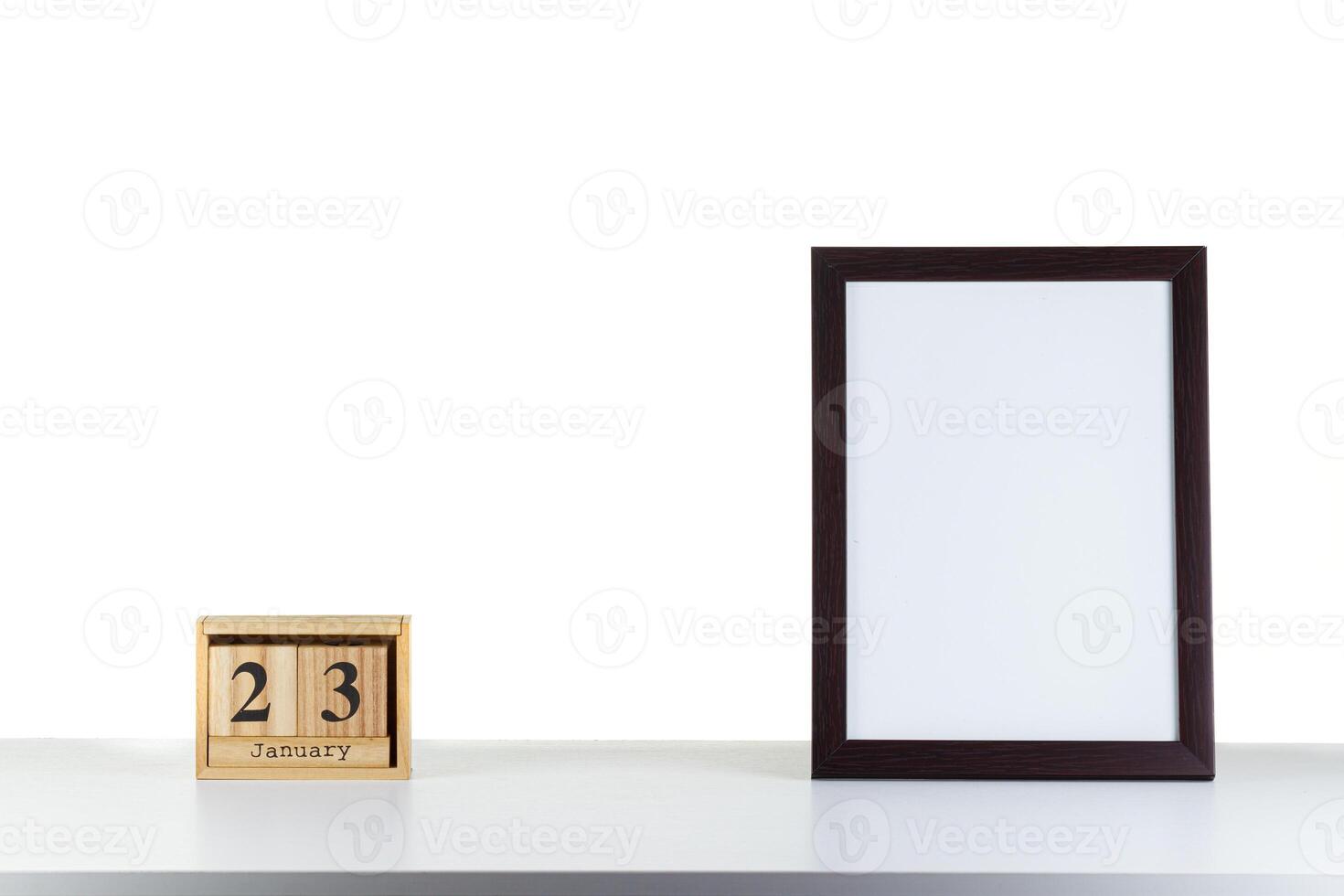 Wooden calendar 23 January with frame for photo on white table and background
