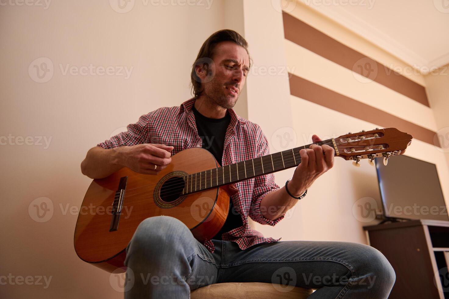 Man playing acoustic guitar in a cozy indoors setting with intent expression photo