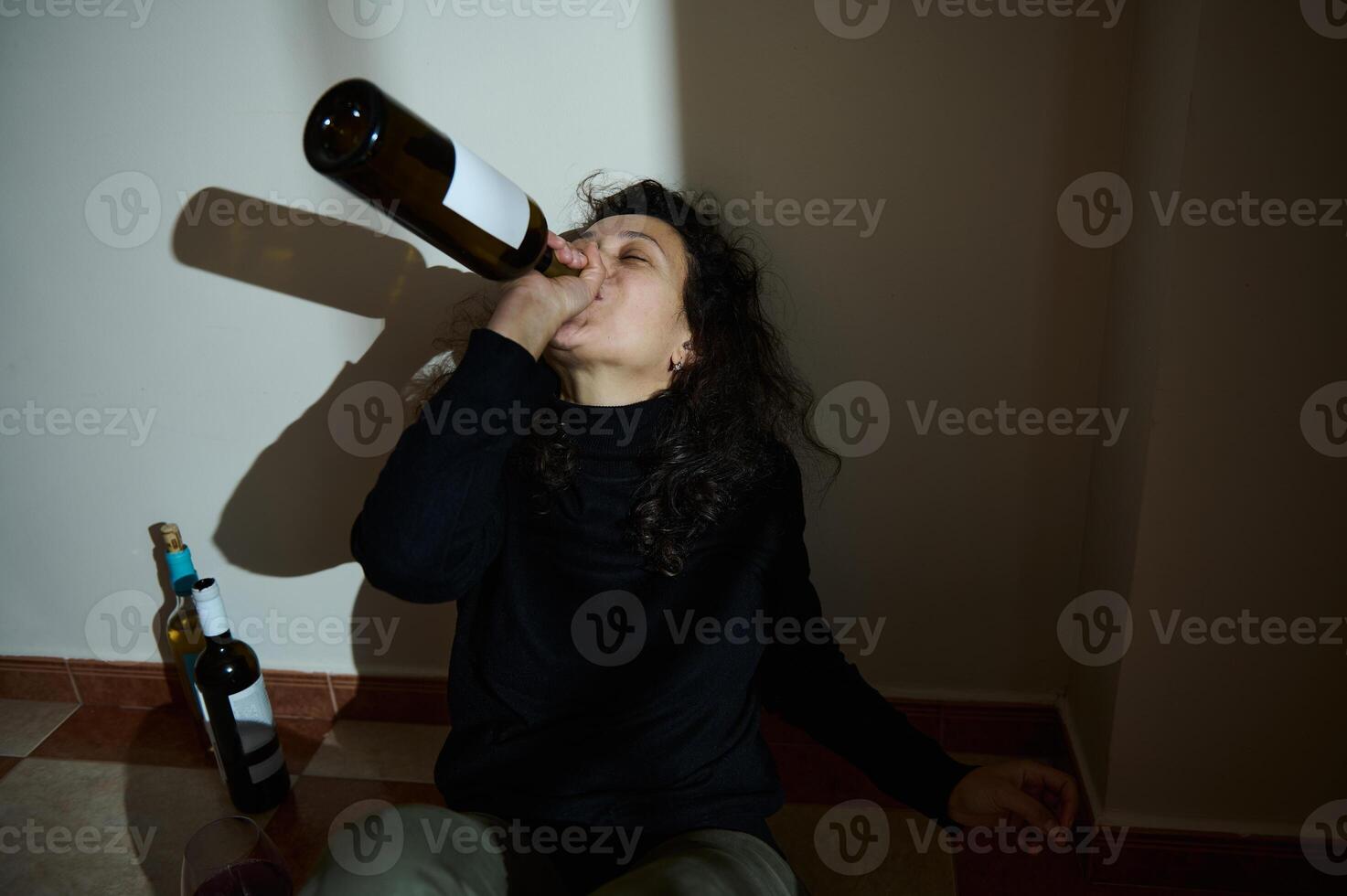 Woman Drinking From A Wine Bottle Sitting Against A Wall photo