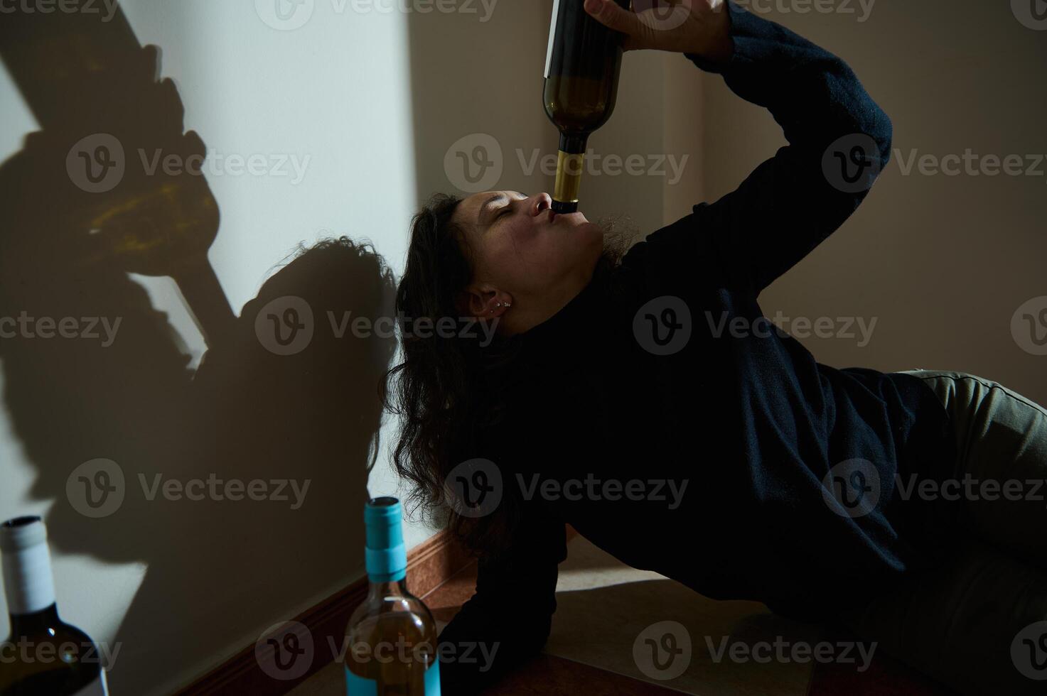 Person drinking from a bottle in a dimly lit setting with shadows photo