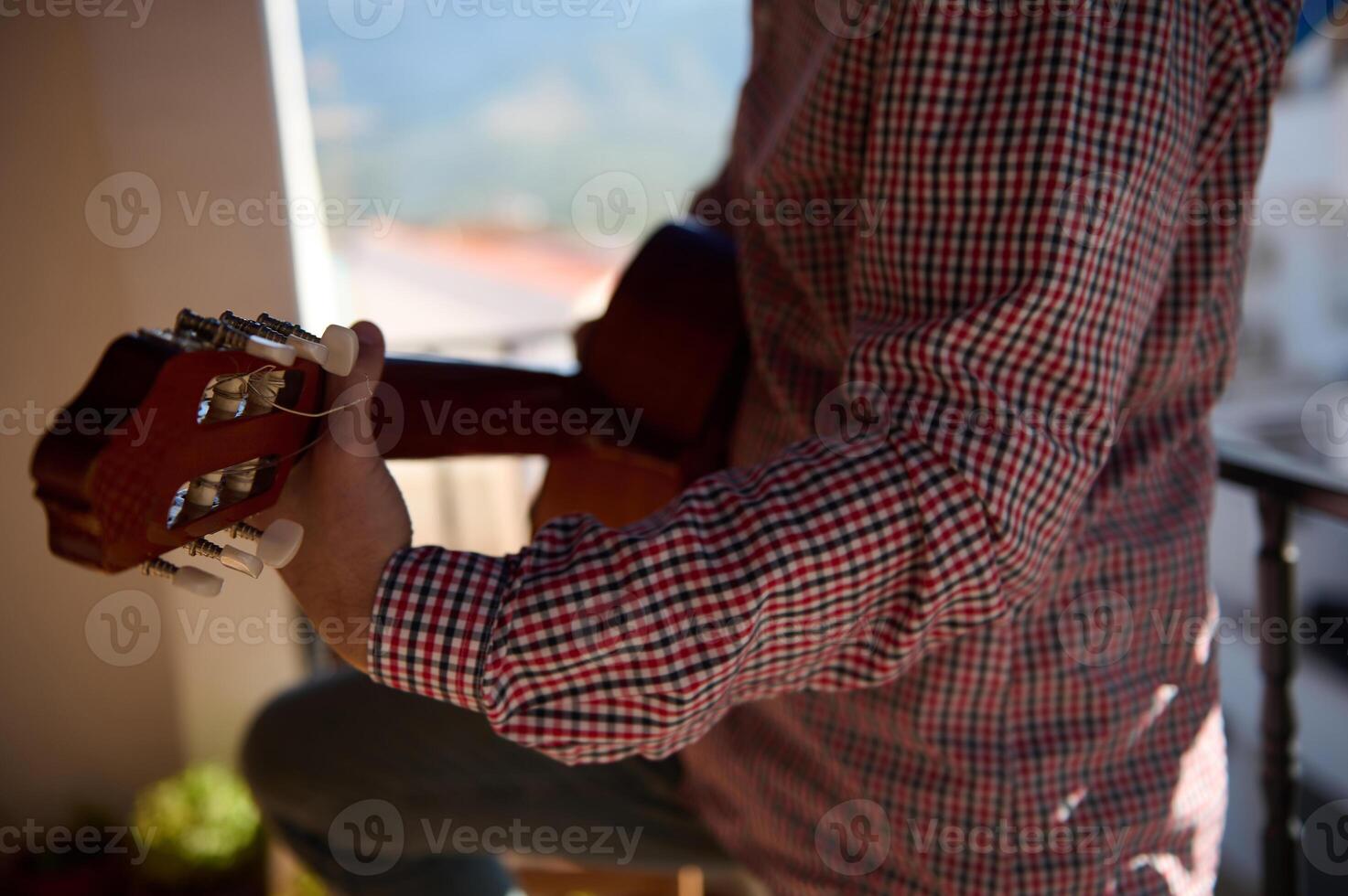 Man playing a guitar on a sunny balcony with scenic background photo