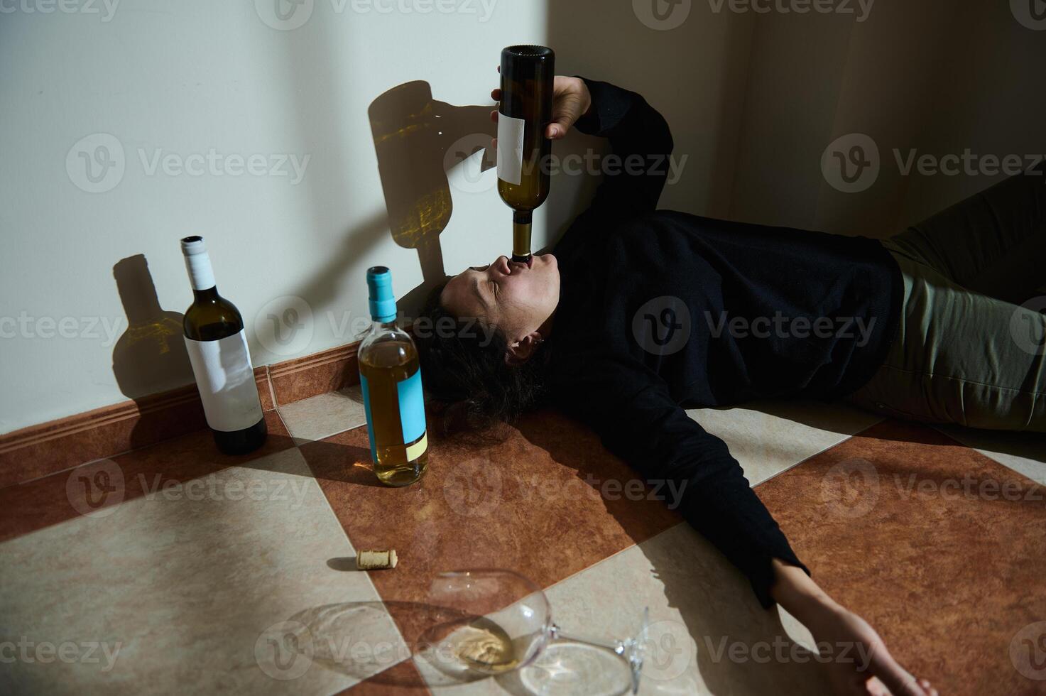 Person laying on tiled floor surrounded by wine bottles photo