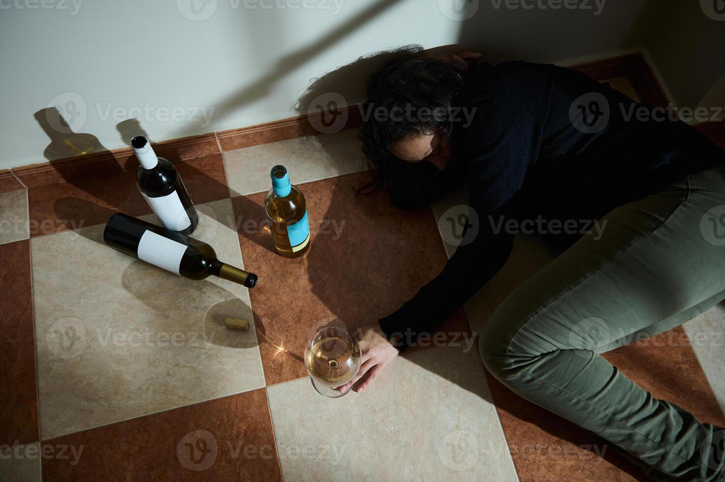 Individual lying on tiled floor surrounded by empty wine bottles photo