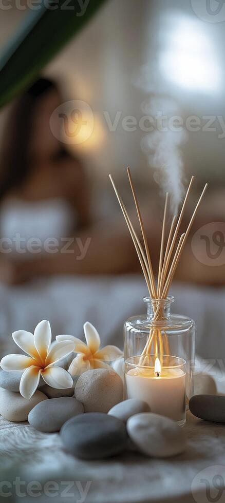 reed diffuser, candles, and rocks on the table, with frangipani flowers beside them photo