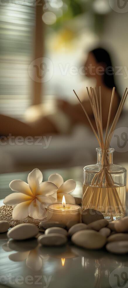 A reed diffuser, candles, and rocks on the table, with frangipani flowers beside them photo