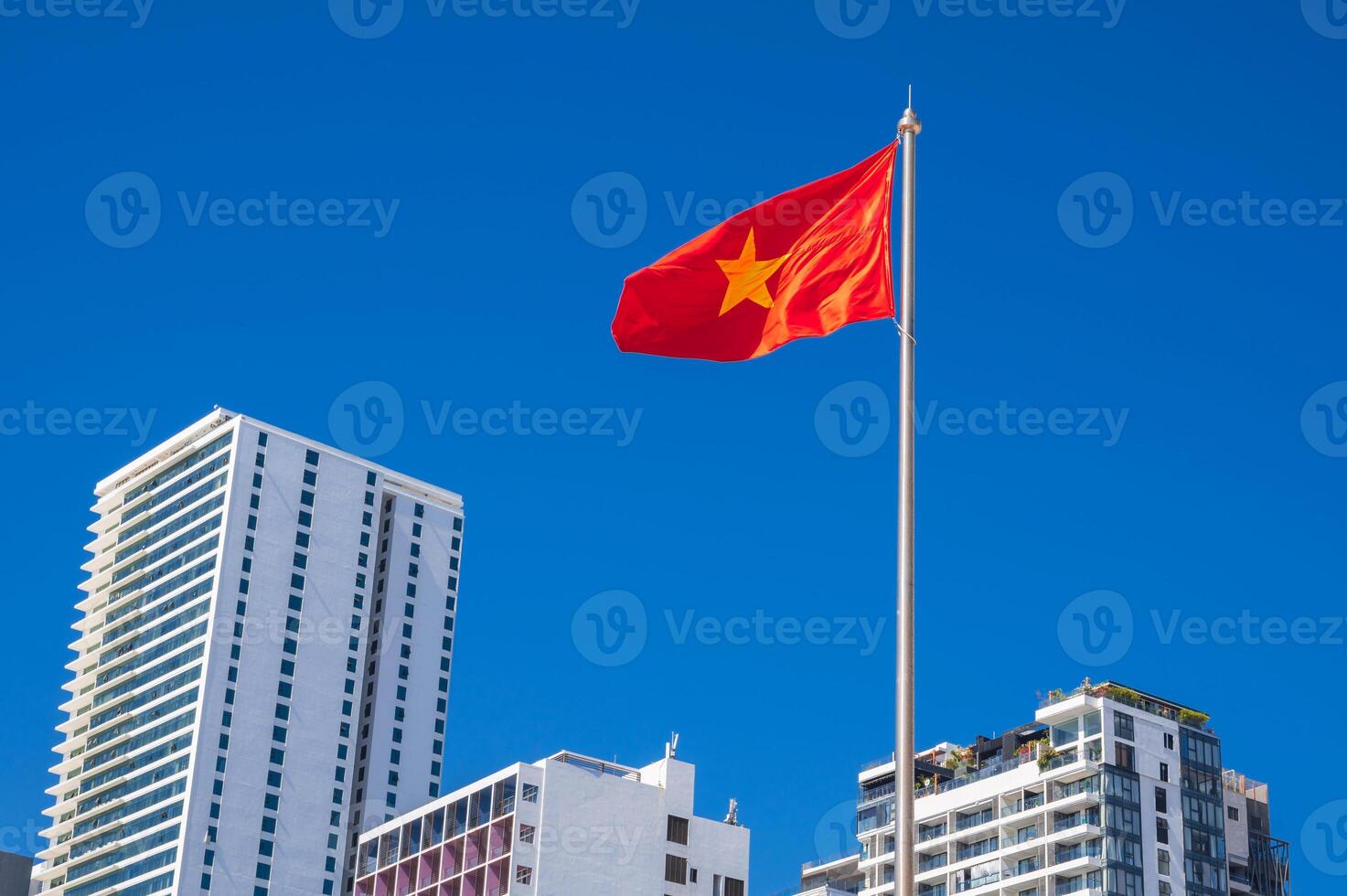 The flag of Vietnam on a flagpole against a background of blue sky and skyscrapers in resort city of Nha Trang in Vietnam photo