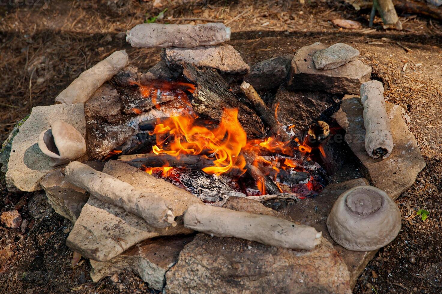 A burning fire surrounded by stones is used to bake clay products in a natural forest empire. photo