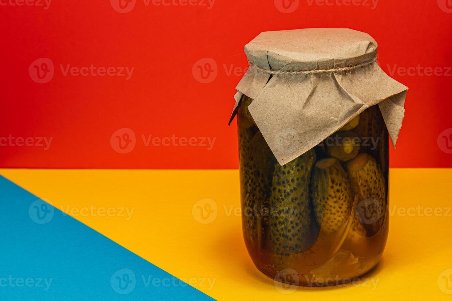 Homemade pickled cucumbers and vegetables in a jar on a colorful background photo
