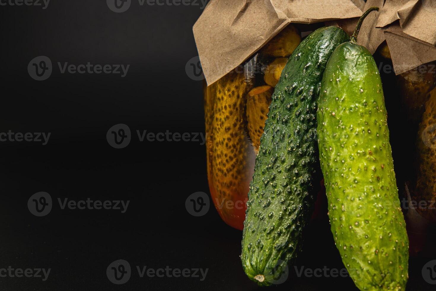 Homemade pickled cucumbers and tomatoes in jars on a dark background photo