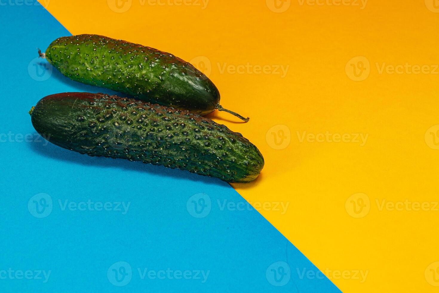 Fresh cucumbers on a vibrant blue and yellow background evoke summer vibes photo